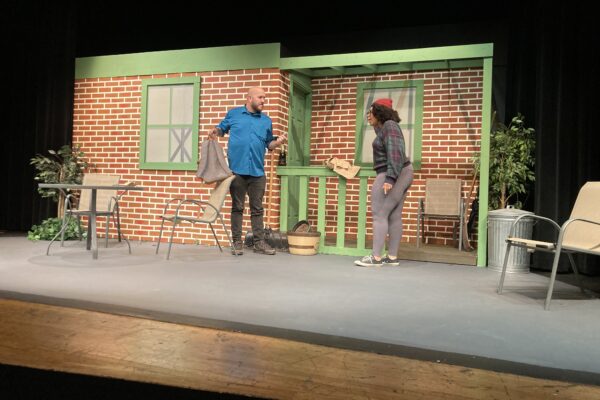 two people talking on a stage set like a brick building